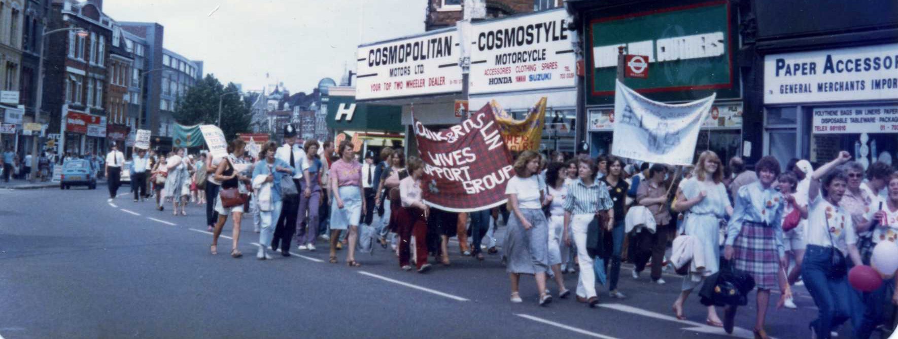 Eine Gruppe Menschen, die meisten von ihnen Frauen, laufen mit Transpis eine Straße entlang. Sie demonstrieren in Unterstützung der streikenden Bergarbeiter. © Wikimedia, https://commons.wikimedia.org/wiki/File:Support_the_Miners_March.Camberwell_Road,_SE5,_London._1984.jpg