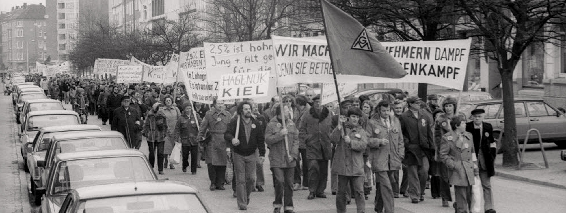  Protestzug der Hagenuk-Mitarbeiter in der Gneisenaustraße. Links neben der IG Metall-Fahne der Erste Bevollmächtigte der IG Metall Kiel Alfred Prezewowsky, dann Harald Carlsen, Betriebsrat bei Hagenuk. Ganz vorn links Betriebsrat Karlheinz Göttsche (links) und rechts der Vorsitzende des Hagenuk-Betriebsrats Günter Schmollmann. © Wikimedia / Stadtarchiv Kiel