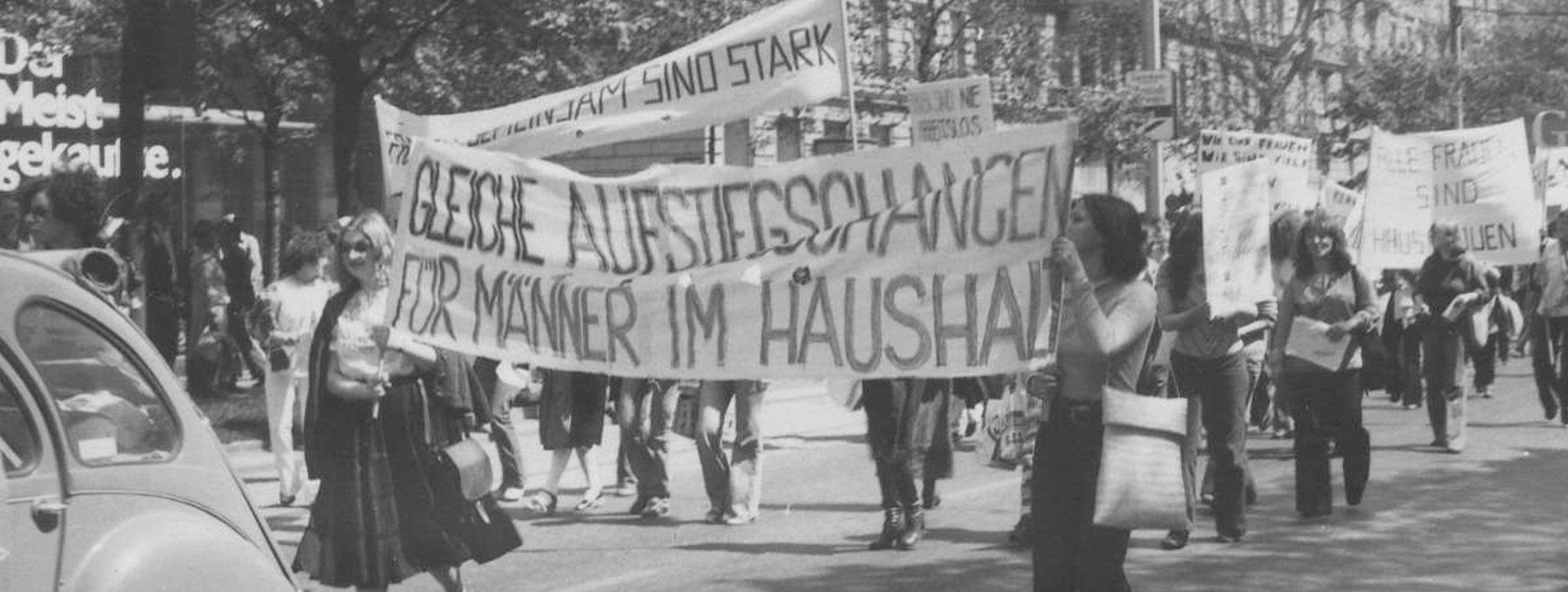 Ein Demonstrationszug, Frauen tragen Banner, auf dem vorne steht "Gleiche Aufstiegschancen f&uuml;r M&auml;nner im Haushalt", weiter hinten "Alle Frauen sind Hausfrauen". &copy; Burgi Hirsch, Kreisky-Archiv