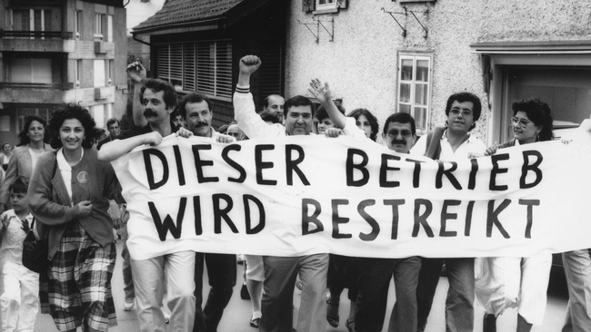 Arbeiter:innen demonstrieren. Vor sich tragen sie ein Transparent mit dem Text Dieser Betrieb wird bestreikt. © Schweizerisches Sozialarchiv F_5031-Fb-0197