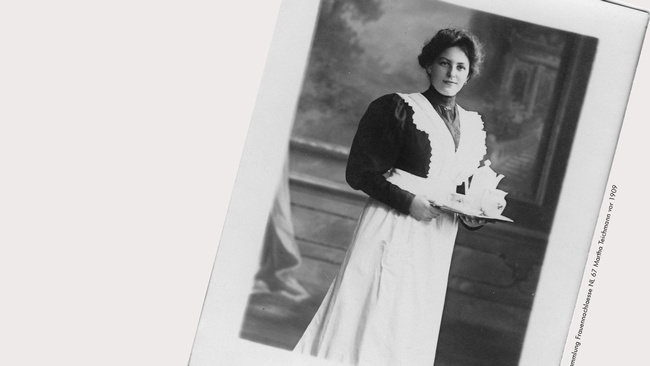 Fotografie einer Frau mit weiner schwarzen Bluse, weißer Schürze, hochgesteckten Haaren. In den Händen hält sie ein Tablett mit Kannen und Tassen. © Sammlung Frauennachlässe, NL 67 Martha Teichmann, vor 1909