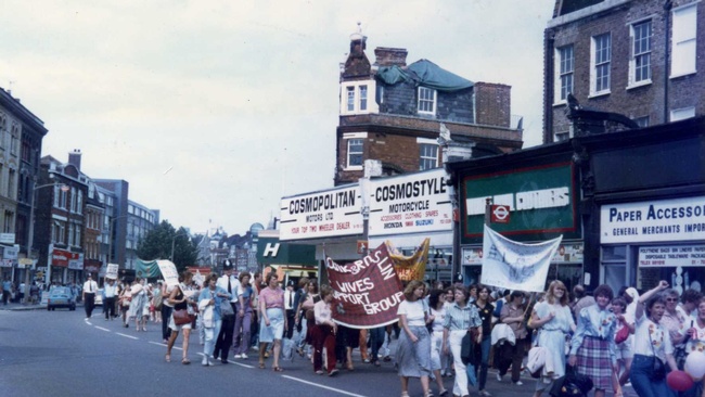 Eine Gruppe Menschen, die meisten von ihnen Frauen, laufen mit Transpis eine Straße entlang. Sie demonstrieren in Unterstützung der streikenden Bergarbeiter. © Wikimedia, https://commons.wikimedia.org/wiki/File:Support_the_Miners_March.Camberwell_Road,_SE5,_London._1984.jpg