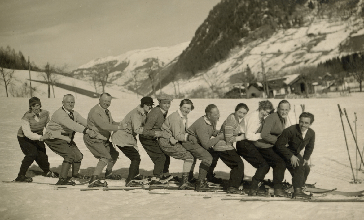 Elf M&auml;nner und Frauen auf Ski stehen aufgereiht auf einer Piste, sie hocken jeweils auf dem Scho&szlig; der Person vor ihnen und schauen in die Kamera. &copy; IHSF-Archiv
