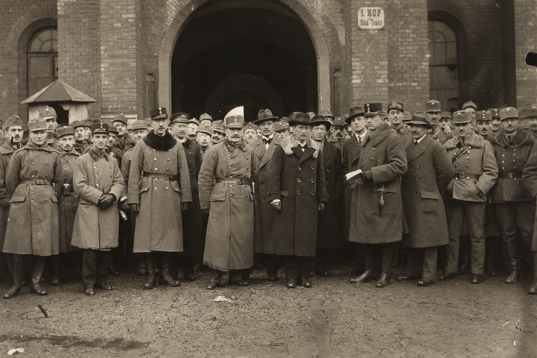 Eine Gruppe M&auml;nner, davon die meisten in MIlit&auml;runiform, schauen Richtung Kamera. In der Mitte steht ein Mann in einem dunklen Mantel, einem Schnurrbart und einem Hut auf. &copy; Richard Hauffe (Fotograf), Wien Museum Inv.-Nr. 49340/89